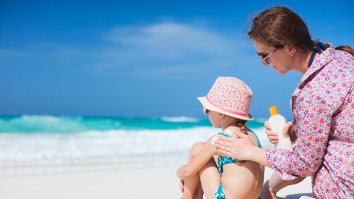 Mom applying reef-safe sunscreen to child at the beach near the ocean.