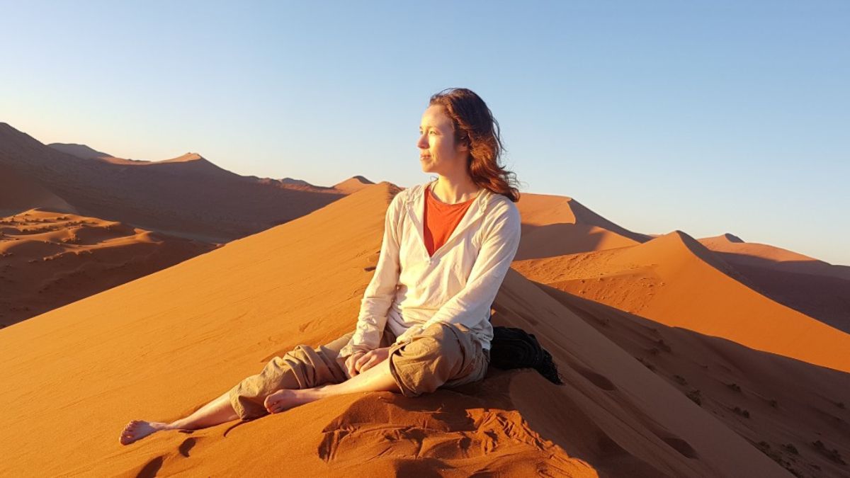 Amanda sits on a sand dune and looks towards the sun