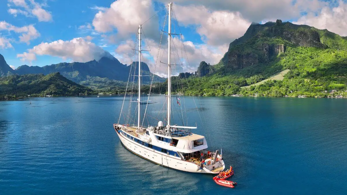 A small cruise boat sails in a bay with a mountainous background