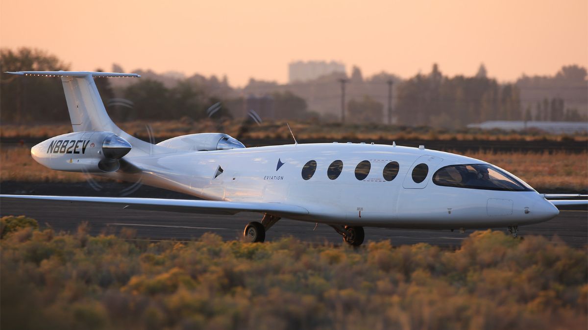 An electric aircraft on a runway at sunset with a city skyline behind