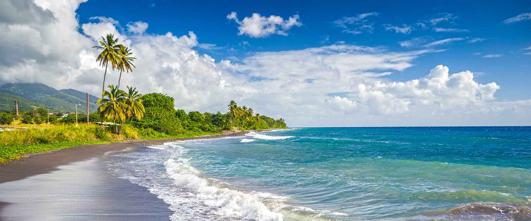 Waves on a black sand beach in St. Kitts, a Caribbean island destination highly vulnerable to climate change that is taking climate action