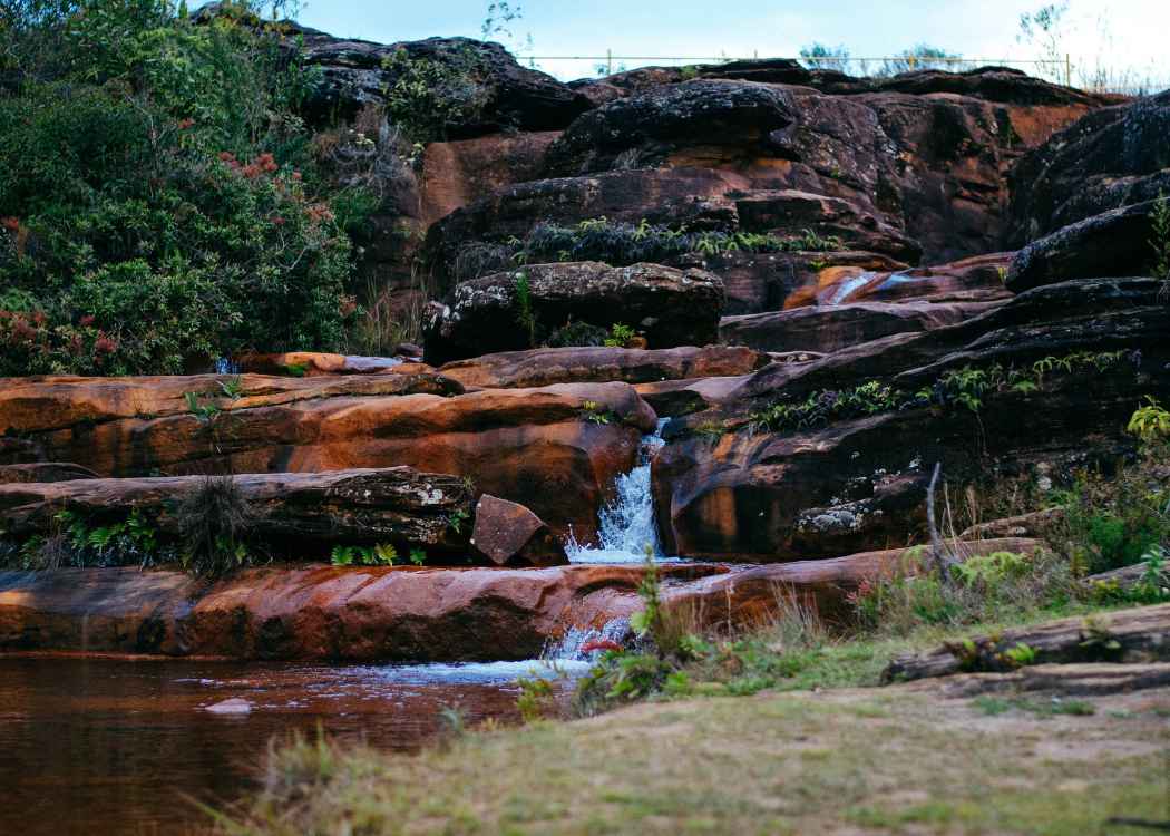 Top view of a calm water cascade in Cachoeira das Andorinhas in Ouro Preto surrounded by greenery and red rocks.