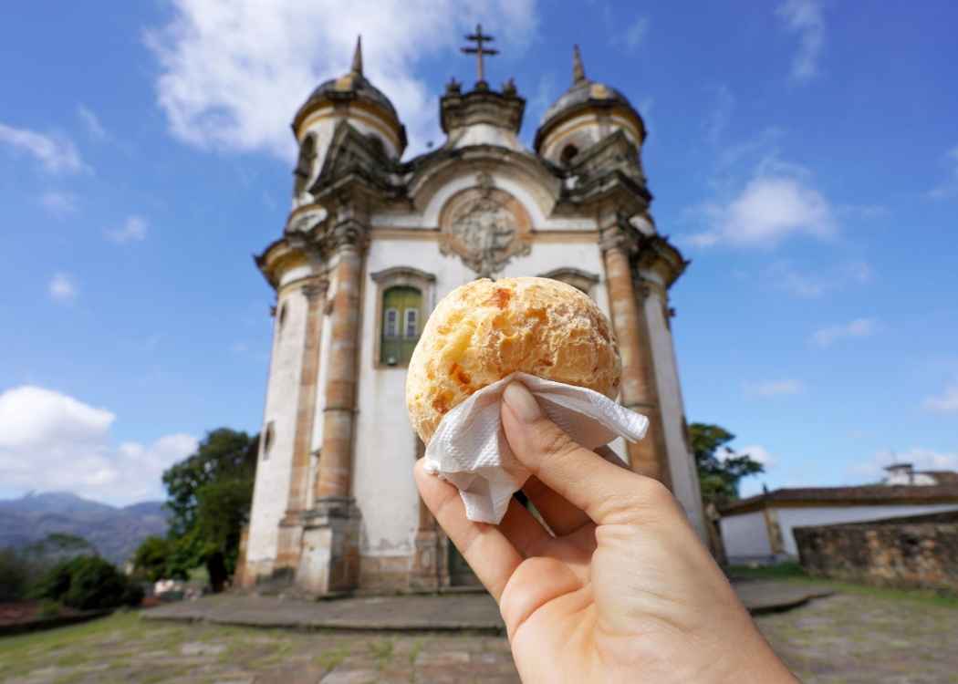 Pao de queijo (Brazilian cheese bun) with the church of St. Francis of Assisi in Ouro Preto, Minas Gerais, Brazil, the city is World Heritage Site by UNESCO